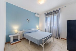 Quarto com cama, mesas de cabeceira, ar-condicionado na parede, cortina e porta.