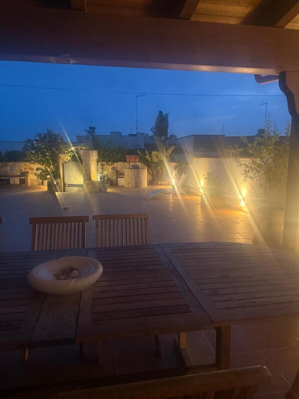 Une terrasse extérieure avec une table et des chaises, un foyer et une vue sur le quartier environnant au crépuscule.