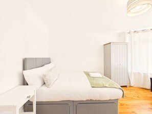 A bedroom with a bed, a nightstand, a wardrobe, and a window with curtains. - Spacious Enfield Stay | Double Garage | Sleeps 6 (Greater London)