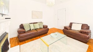 A living room with two brown leather sofas, a glass coffee table, a white fireplace, and a chandelier.