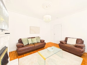 A living room with two brown leather sofas, a glass coffee table, a white fireplace, and a chandelier.