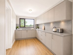 A modern kitchen with a window, grey cabinets, and a countertop with a kettle and toaster. - Spacious Enfield Stay | Double Garage | Sleeps 6 (Greater London)