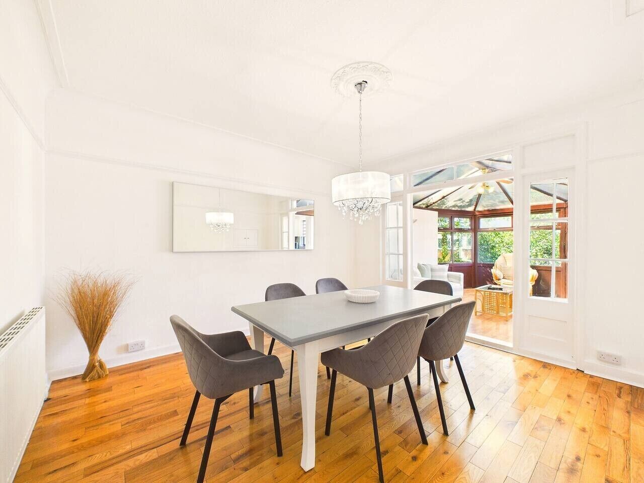 A dining area with a table and chairs, a chandelier, and a view through an open door to an outdoor space.