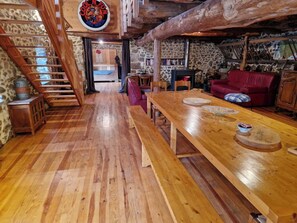 A rustic interior with a wooden staircase, a long dining table, and a stone wall.