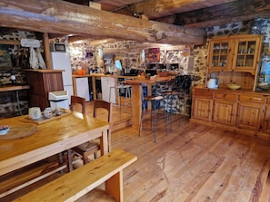 A rustic kitchen with stone walls, wooden furniture, and a bar area. - Charming stone and wood gîte with large capacity (Mazeyrat d'Allier)
