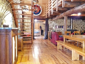 A rustic interior with a wooden staircase, stone walls, a fireplace, and a dining area.