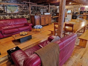 A cozy living area with a red leather sofa, wooden coffee table, and a dining table with benches. - Charming stone and wood gîte with large capacity (Mazeyrat d'Allier)