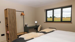 A bedroom with a bed, a desk, a mirror, a hanging clothes rack, and a window with a view of a field. - The Cozie Sow (Yeovil)