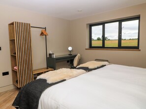 A bedroom with a bed, a desk, a mirror, a hanging clothes rack, and a window with a view of a field.