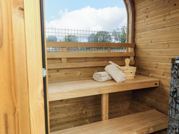 A wooden sauna with a bench, a towel, and a wooden bucket.