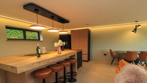 A modern kitchen with a wooden bar, bar stools, and a dining area with a table and chairs. - The Cozie Sow (Yeovil)