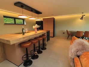 A modern kitchen with a wooden bar, bar stools, and a dining area with a table and chairs.