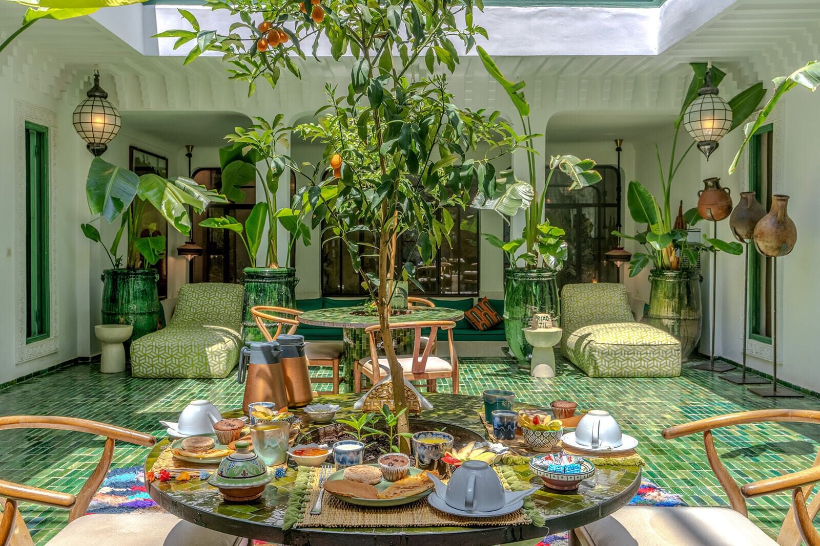 Un patio con una mesa puesta para comer, rodeado de sillas y plantas en macetas.