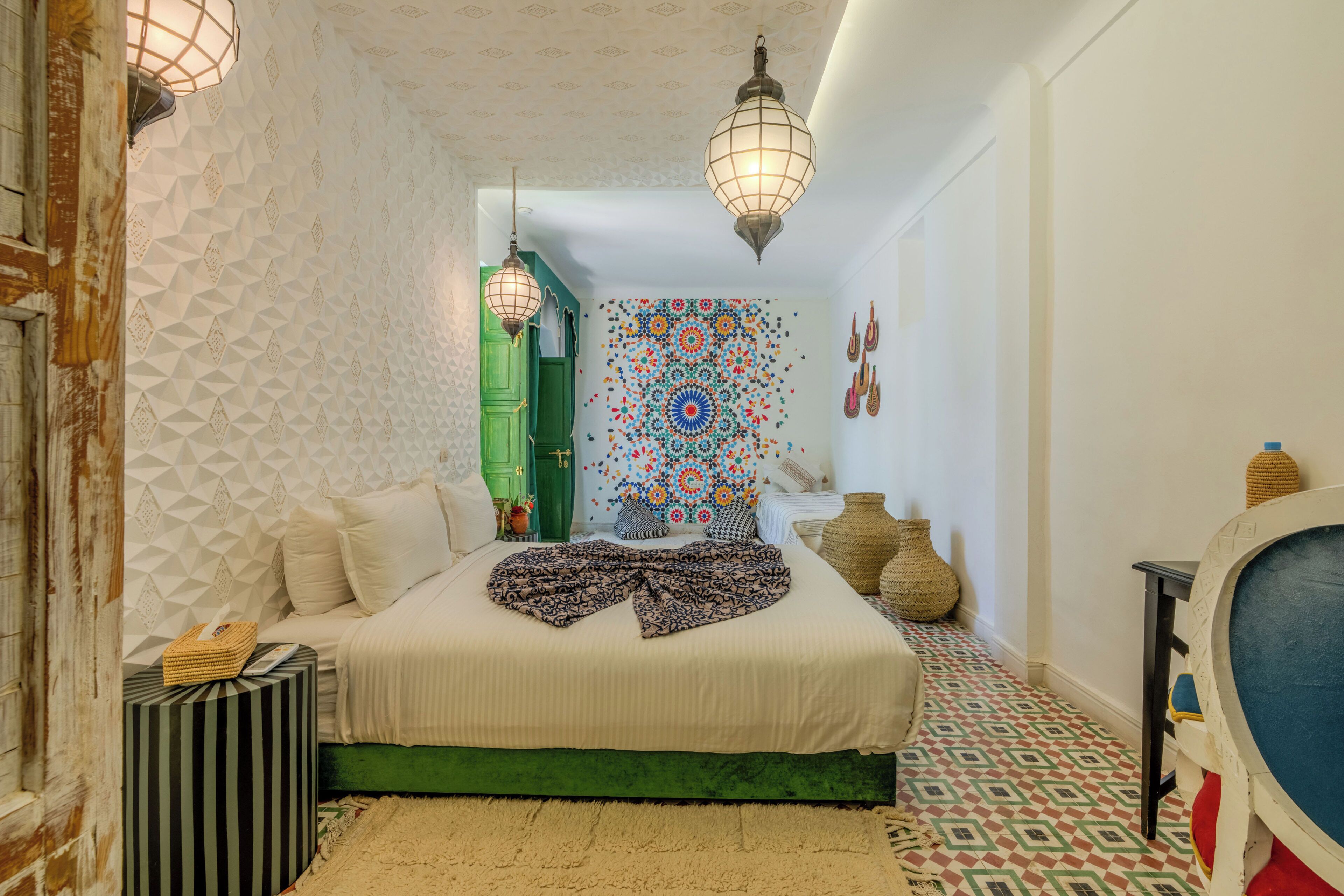 A bedroom with a bed, a green door, a patterned wall, and hanging lights.