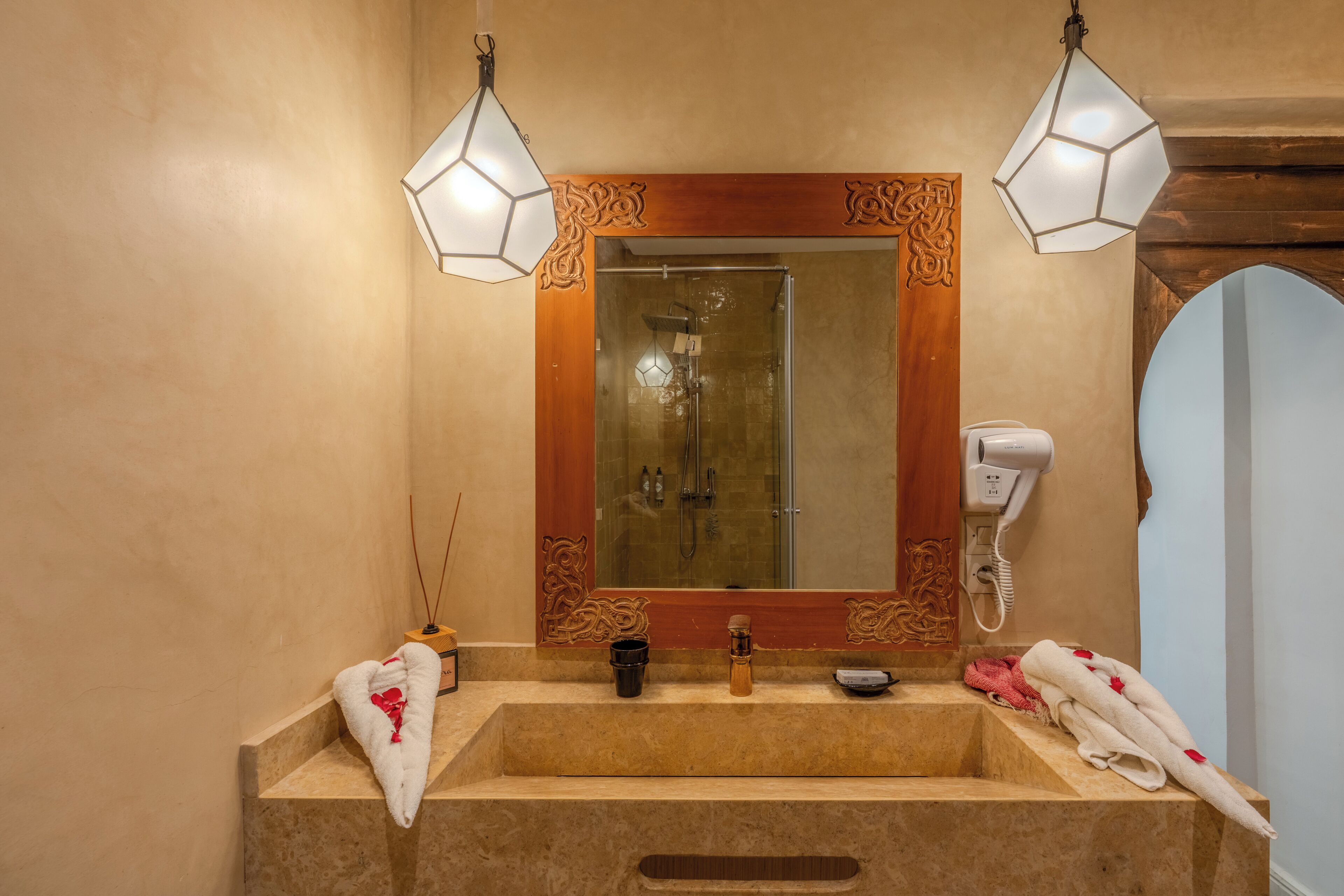 A bathroom with a large mirror, two pendant lights, a hairdryer, and towels on the counter.