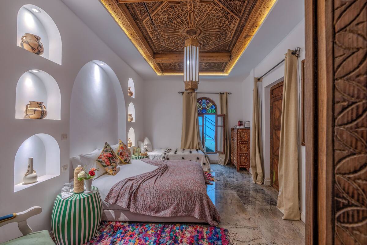 A bedroom with a bed, a window with curtains, a decorative ceiling, and a wooden door.
