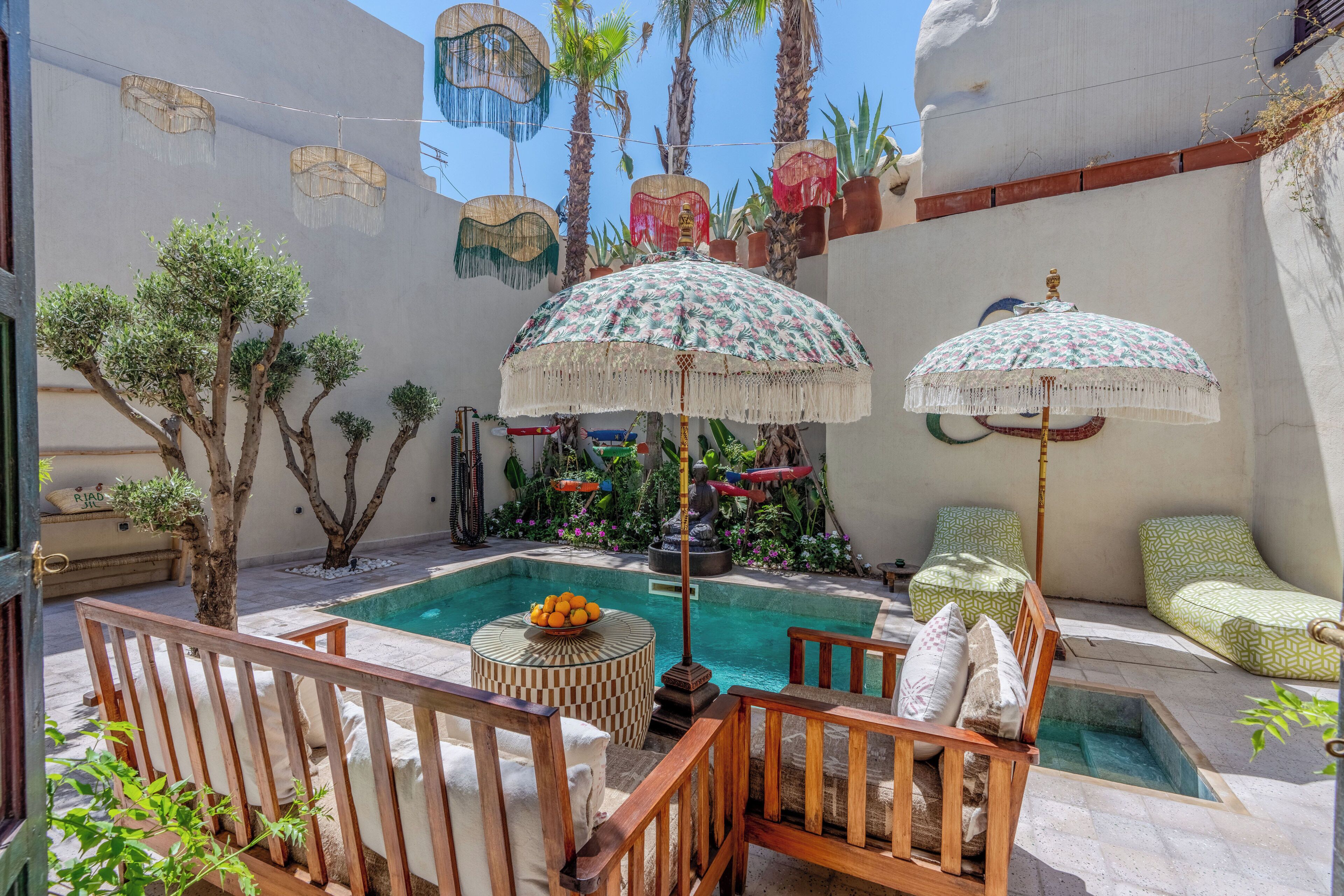 Zona de piscina con sillones de descanso, sombrillas y una pequeña mesa con fruta.