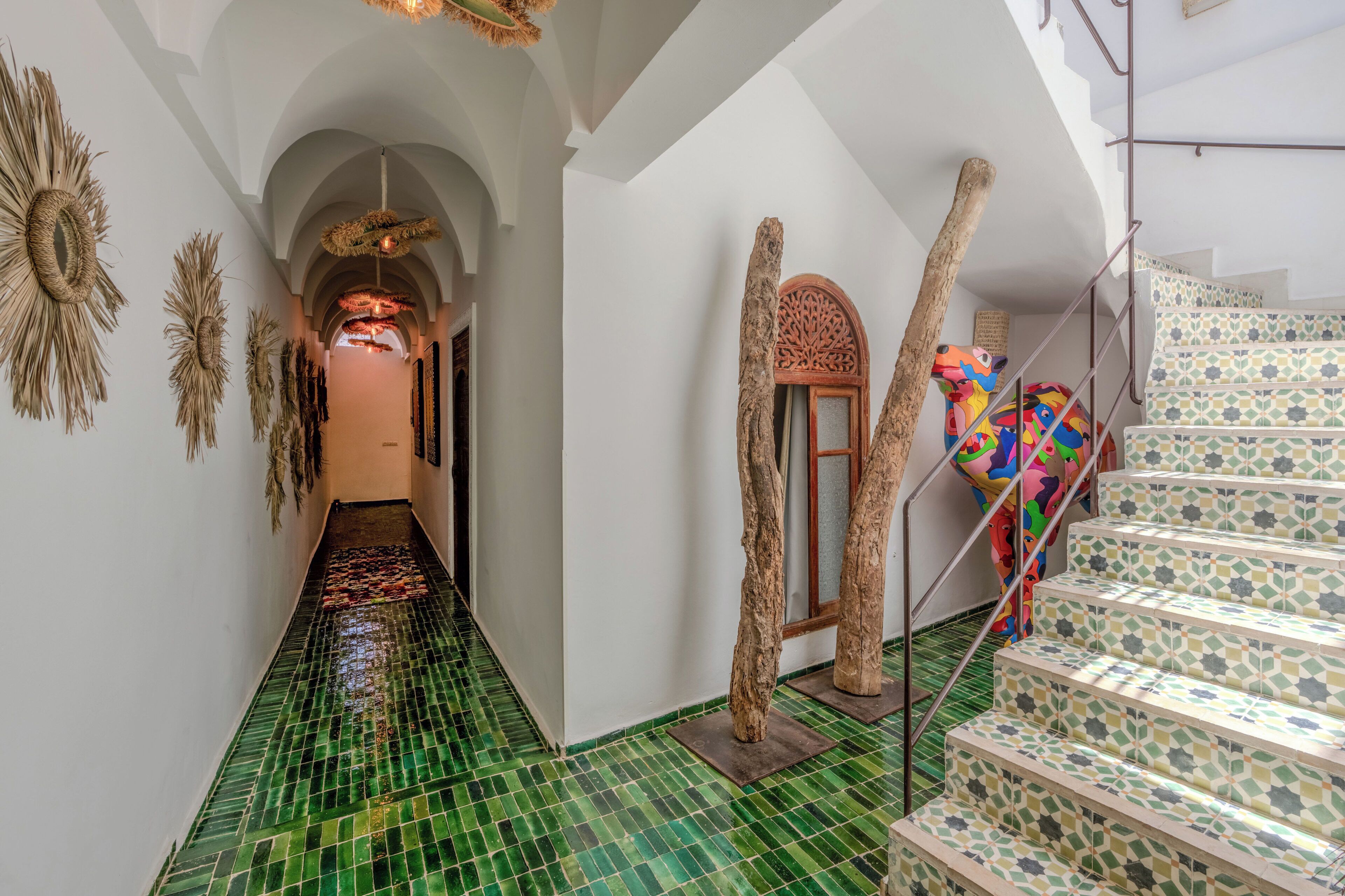 A hallway with green tiled flooring, a staircase with patterned steps, and decorative wall art.