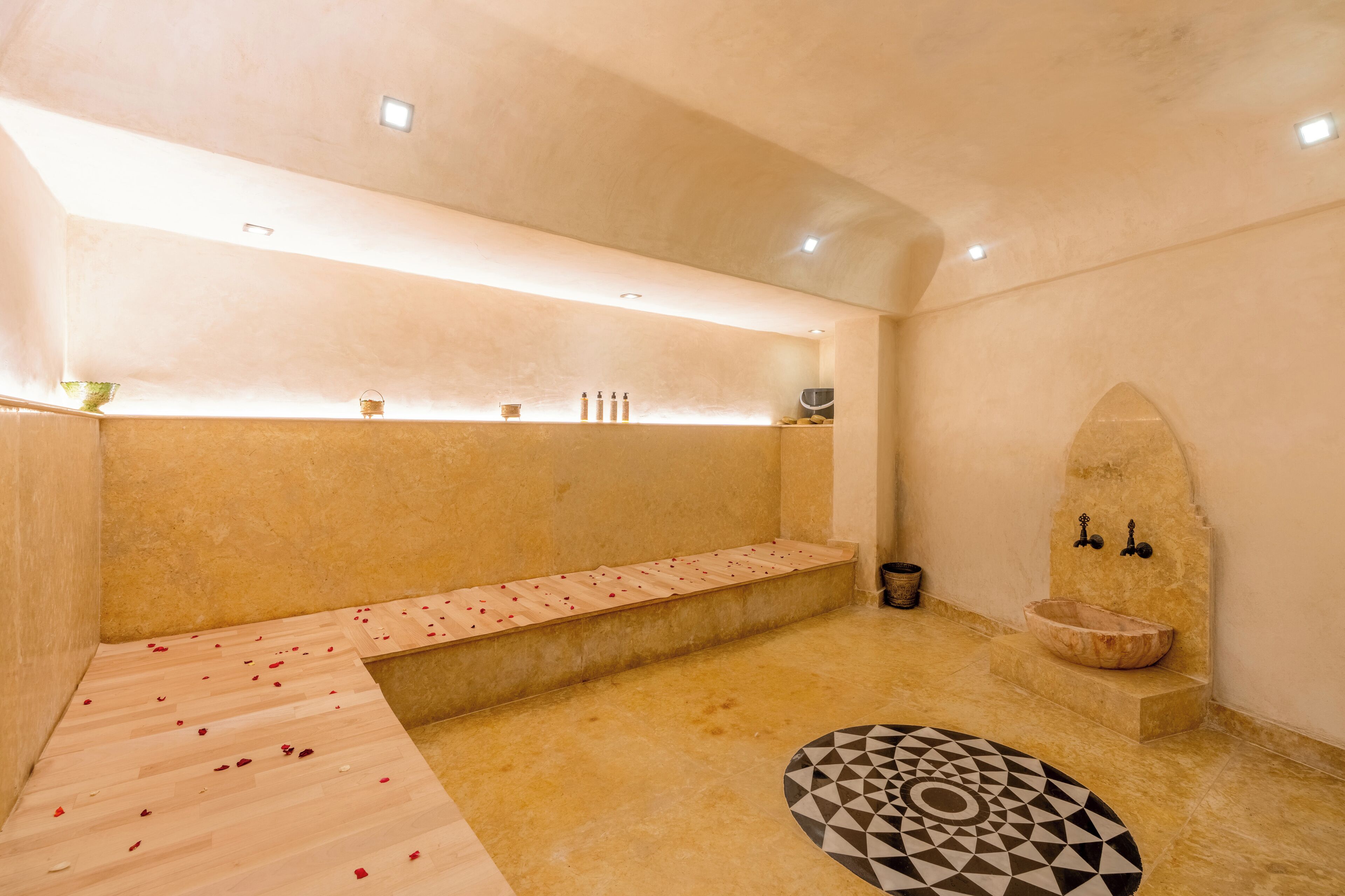 A spa room with a wooden bench, a stone basin, and a geometric-patterned rug.