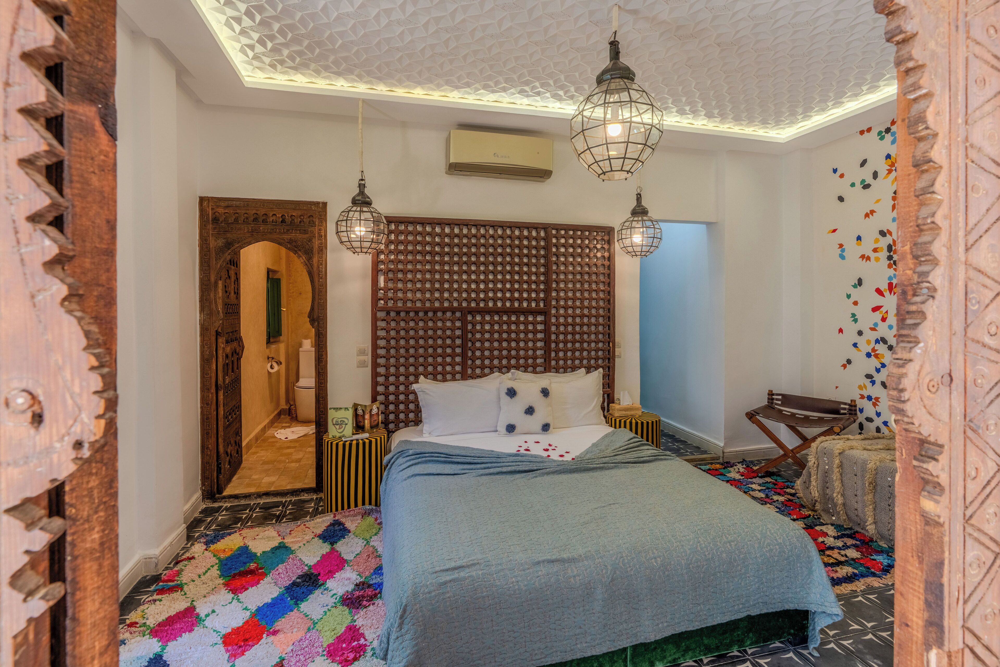 A bedroom with a bed, a wooden headboard, a patterned rug, and hanging light fixtures.