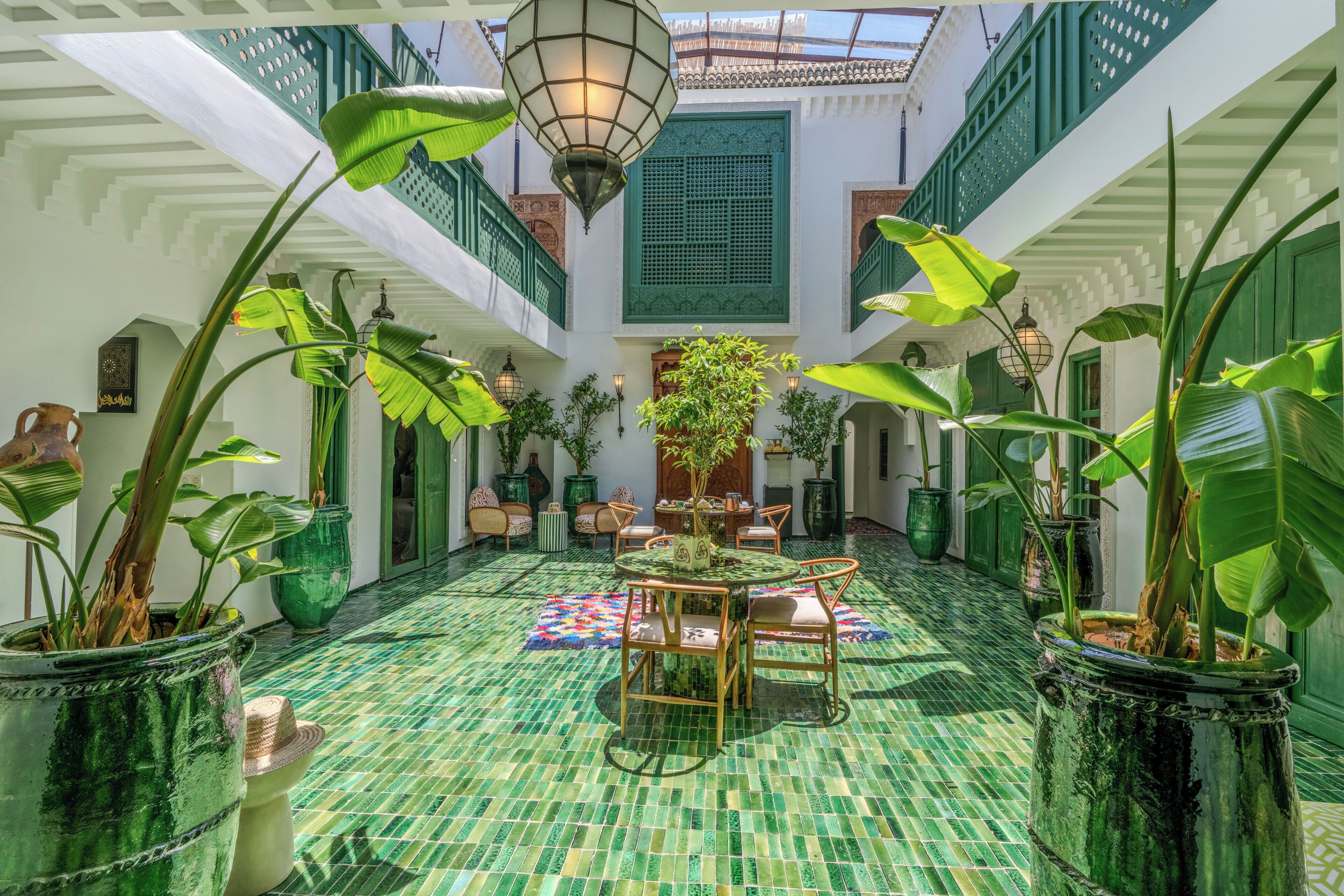 A courtyard with a tiled floor, potted plants, a round table with chairs, and a hanging lantern.