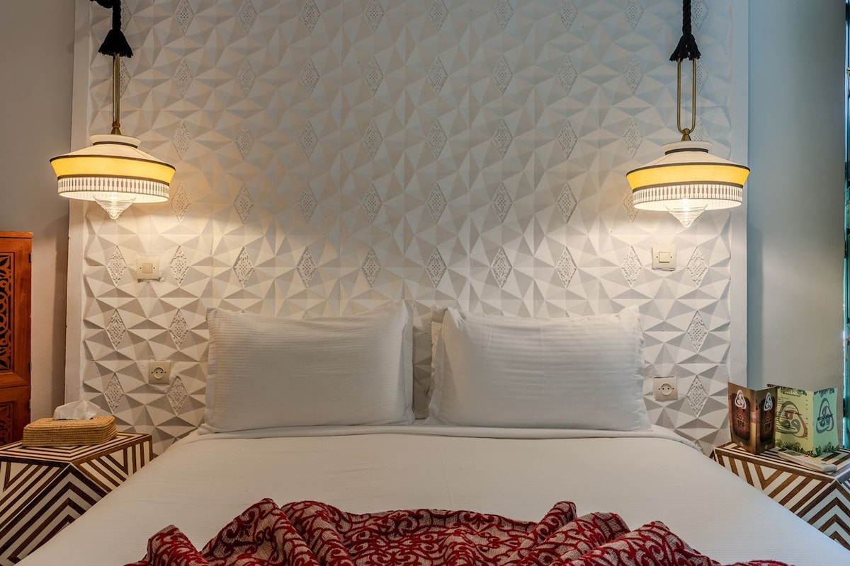 A bed with a geometric patterned headboard, two bedside lamps, and a patterned throw blanket.