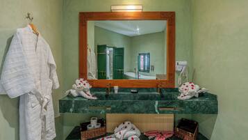 A bathroom with a green marble sink, a large mirror, and a robe hanging on the wall.