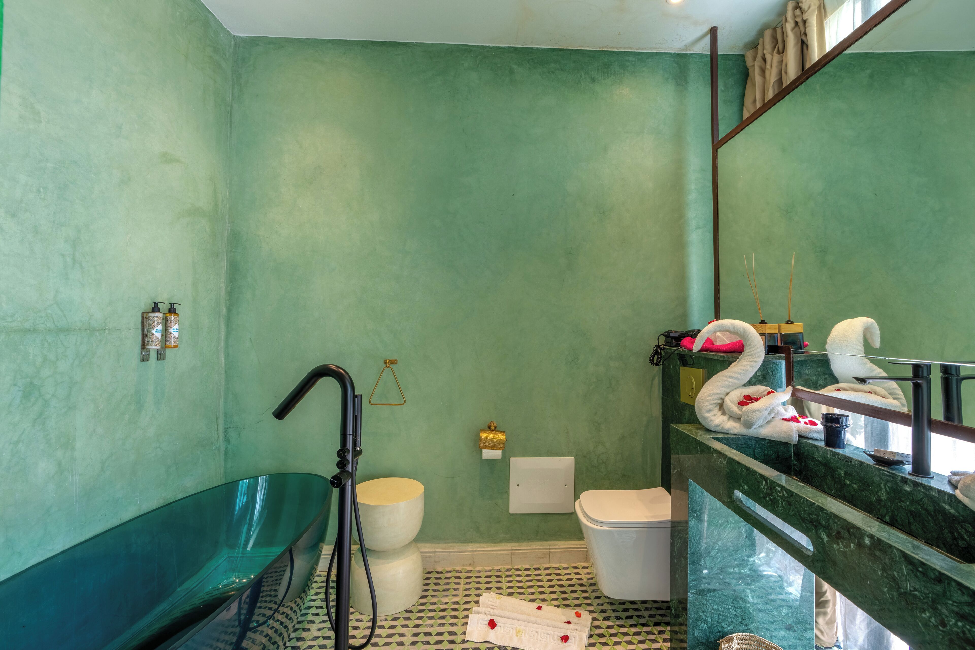 Une salle de bain avec un mur vert, une baignoire sur pieds, des toilettes et un lavabo doté d’un plan de travail en marbre.