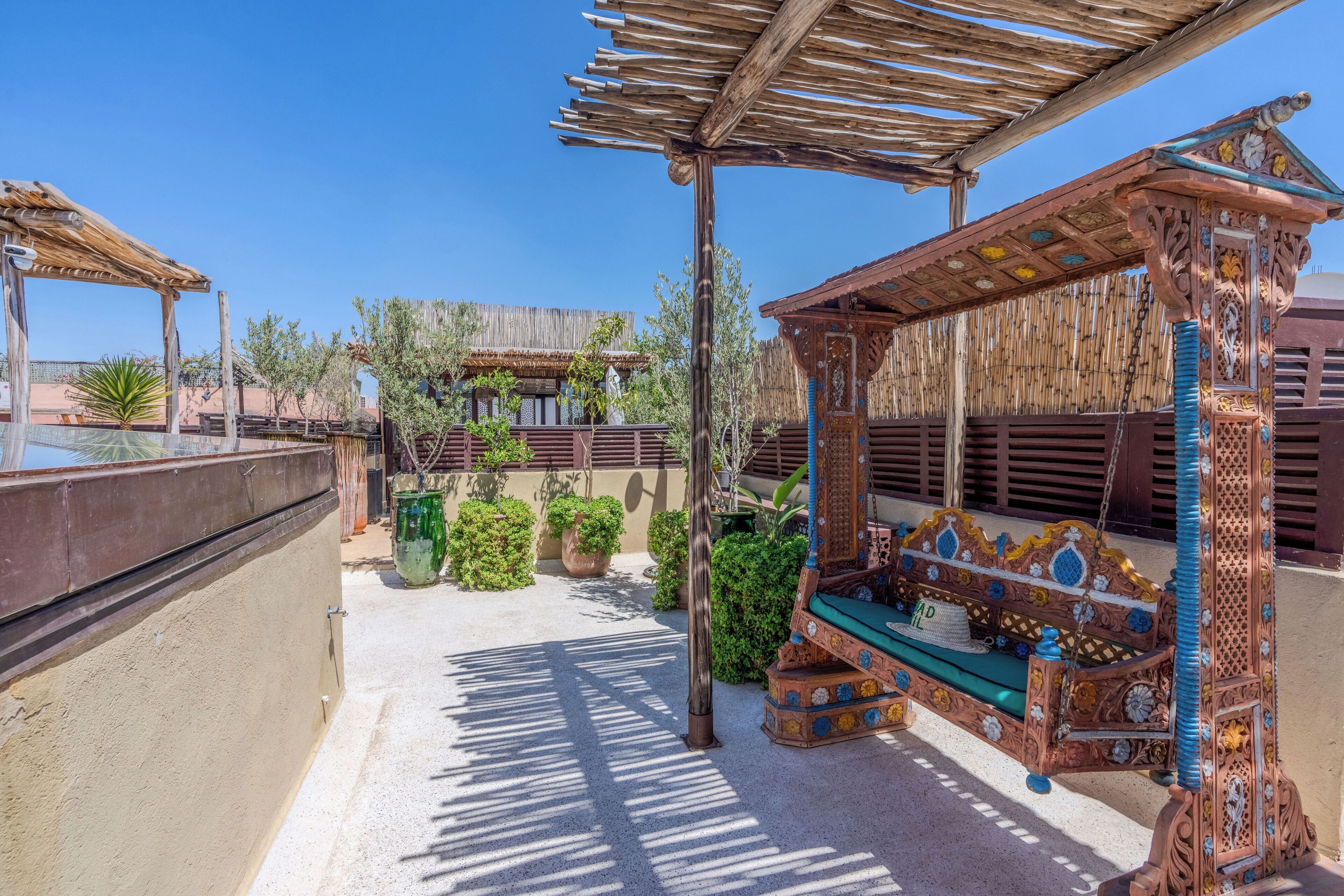 A courtyard with a wooden swing, a pergola, and a wall with a textured pattern.