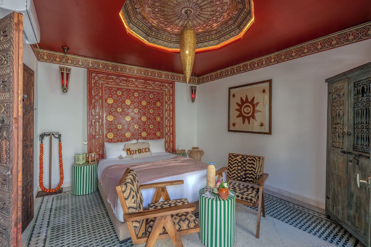 A traditional Moroccan room with a patterned bed, a wooden chair, a cabinet, and a decorative ceiling.