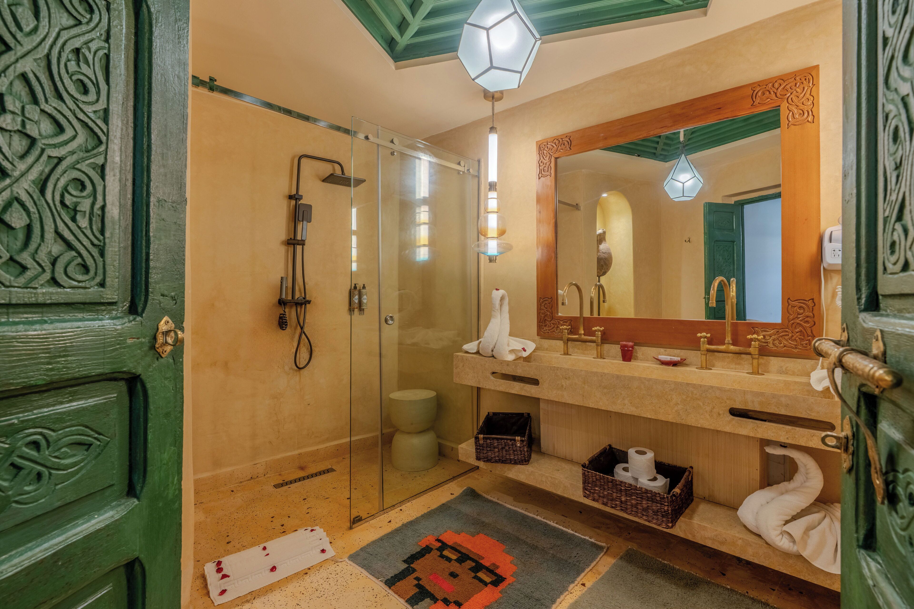 A bathroom with a glass shower enclosure, a large mirror, and a green door with intricate carvings.