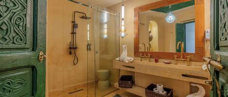 A bathroom with a glass shower enclosure, a large mirror, and a green door with intricate carvings.