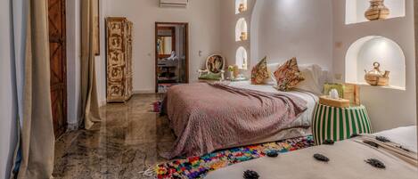 A room with a bed, a small table, a mirror, and a decorative ceiling.
