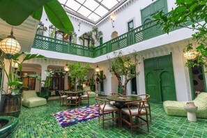A courtyard with a green mosaic floor, a dining area with chairs and a table, and a green balcony with plants. - Riad Jil & Spa Marrakech  (Marrakech)
