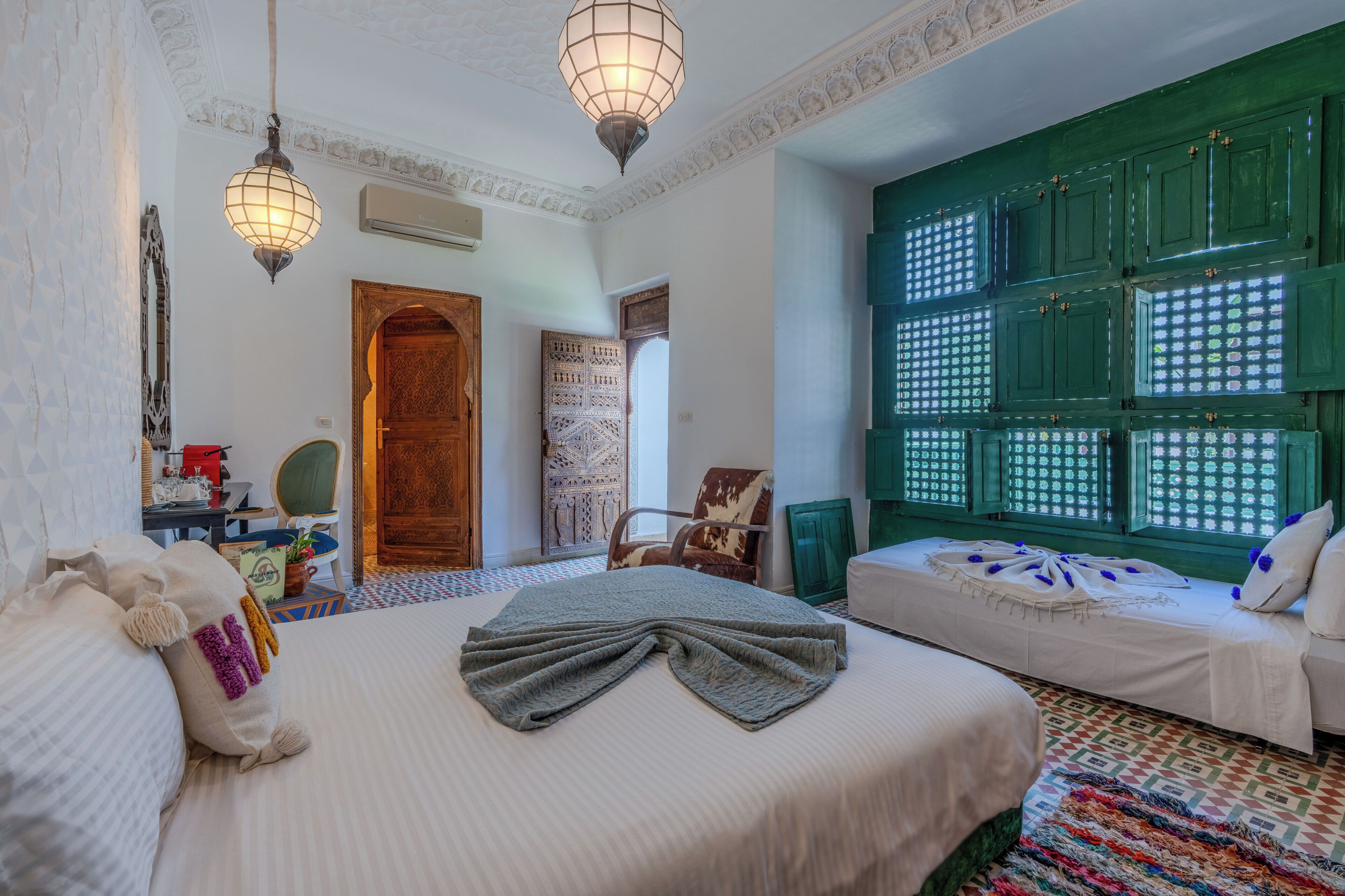 Una habitación con una cama, una silla, un escritorio y una pared verde con ventanas.