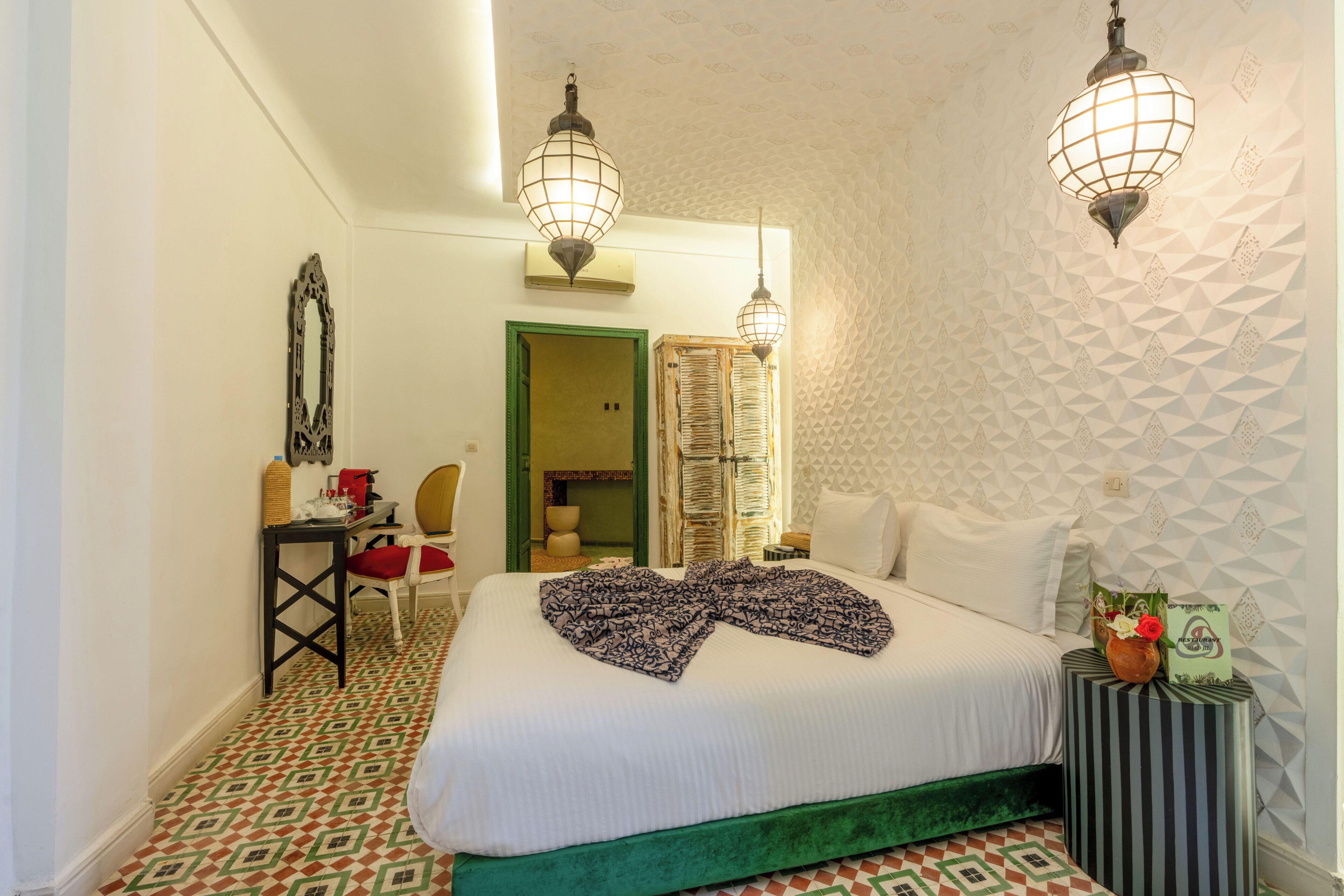 Una habitación de hotel con cama, escritorio, silla, lámpara y pared con diseño.