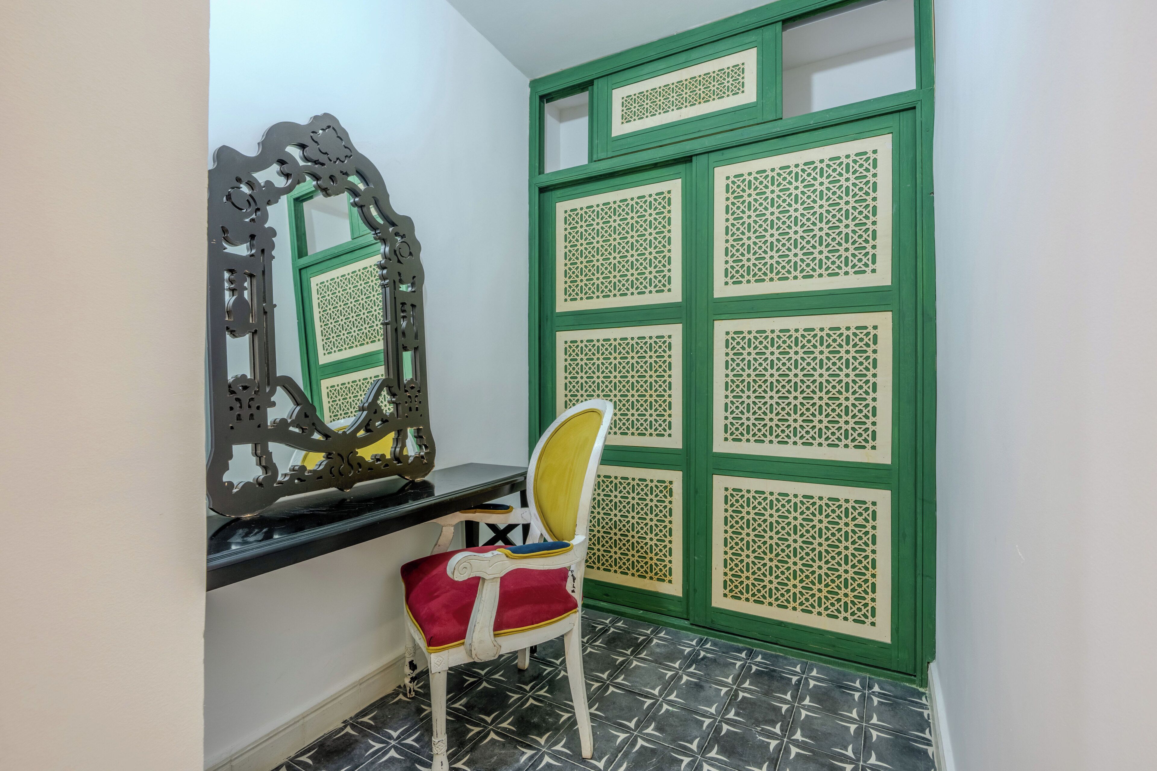 A room with a chair, a decorative mirror, and a green partition with intricate patterns.