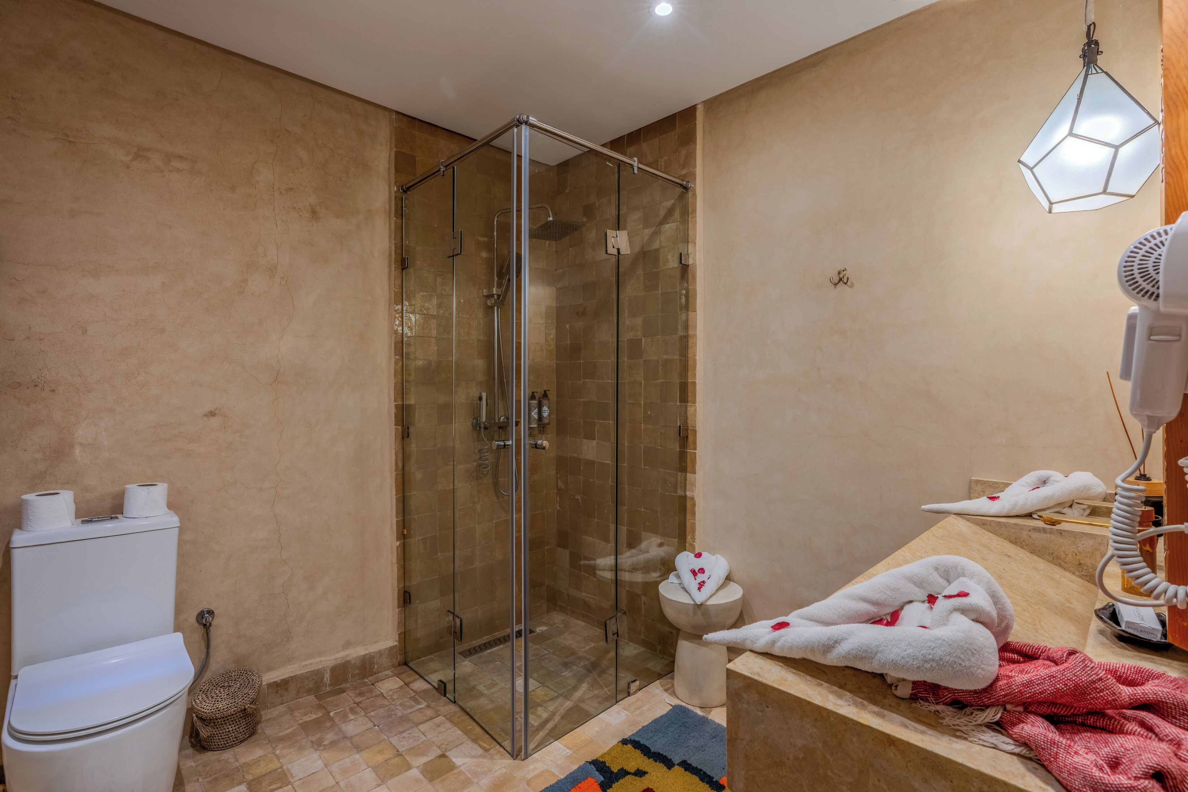 A bathroom with a glass-enclosed shower, a toilet, a sink with a towel, and a hairdryer.