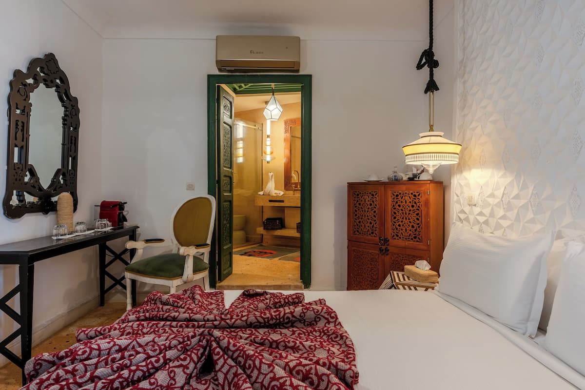 A hotel room with a bed, a desk, a chair, a wardrobe, and an open door leading to a bathroom.