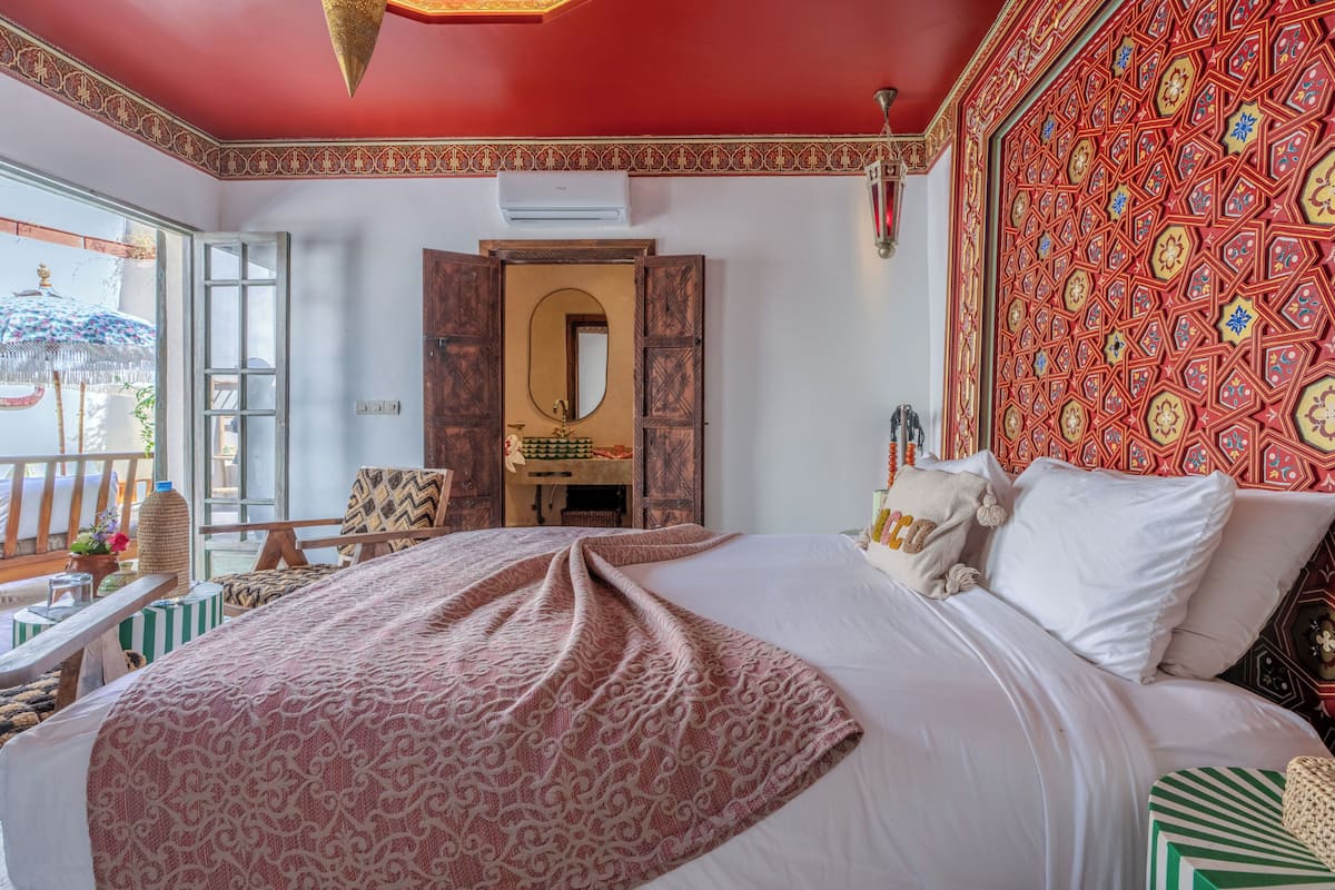 A room with a bed, a mirror, a window, and a patterned wall.