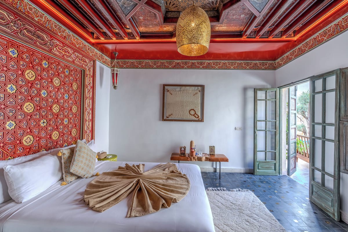 A room with a bed, a table with items, a hanging light, and a door leading outside.