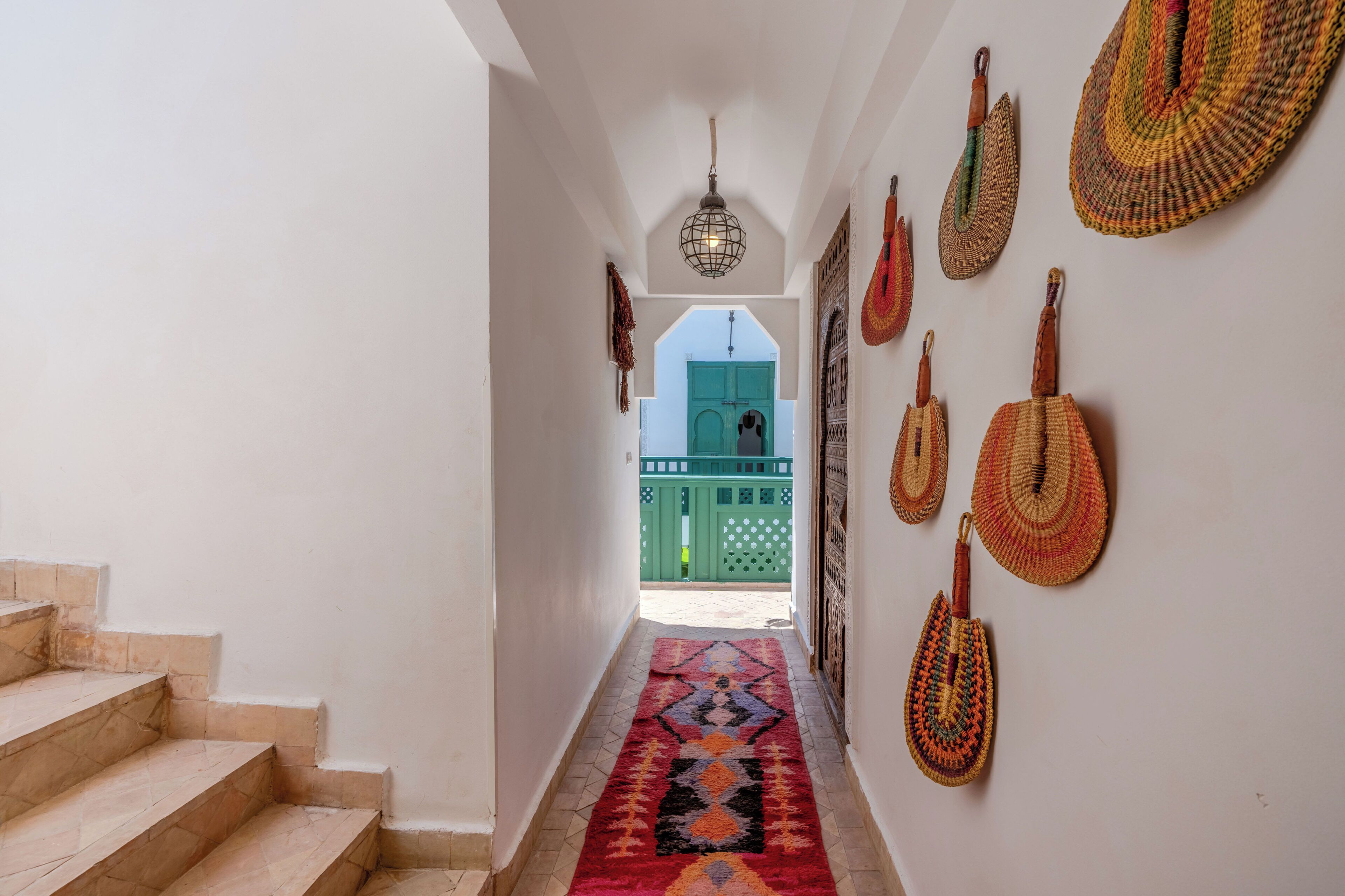 A hallway with a patterned carpet, a staircase, and decorative woven items on the wall.