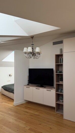 A modern living room with a flat-screen TV, a chandelier, a bookshelf, and a skylight. - Scandinavian Skylight Loft - Riga Quiet Center - Historic Building, AC (Rīga)