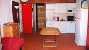 Una cuina compacta amb taula de menjador, armaris blancs, microones i nevera.