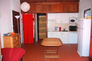 Eine kleine Küche mit Esstisch, weißen Schränken, einer Mikrowelle und einem Kühlschrank.