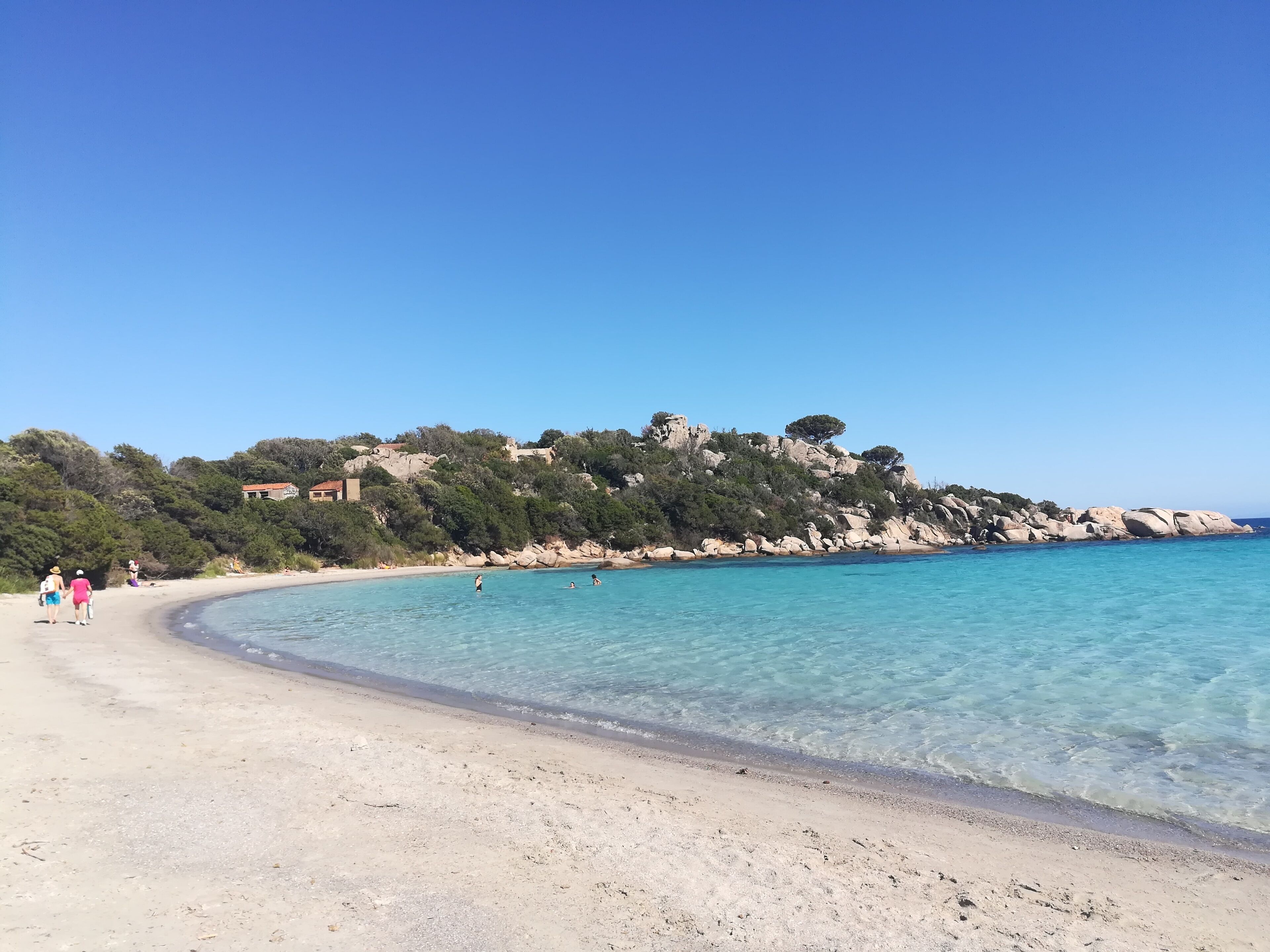 A beach with clear turquoise water, a sandy shore, and rocky cliffs with vegetation.
