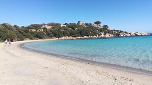 Una platja amb aigua turquesa cristal·lina, un tram de sorra i penya-segats rocosos amb vegetació.