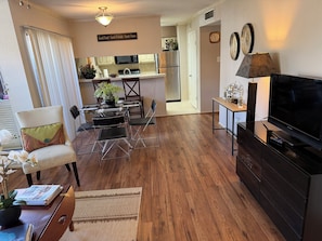 A living room with a TV, a dining area with chairs and a table, a kitchen with appliances, and a hallway. - Houston TX - Houston Stadium - 2Be/2Ba Condo - WORLD CUP!!! (Houston)