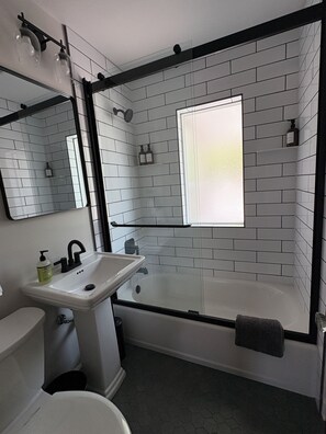 Et badeværelse med en hvid vask, et spejl, et toilet og et badekar med et vindue.