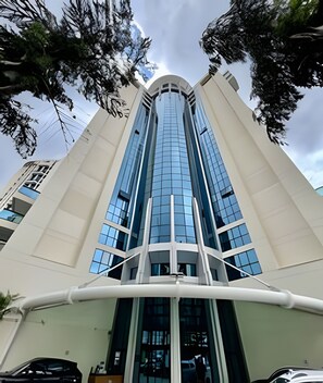 Un edificio alto y moderno con fachada de vidrio, elementos estructurales blancos y una entrada curva.